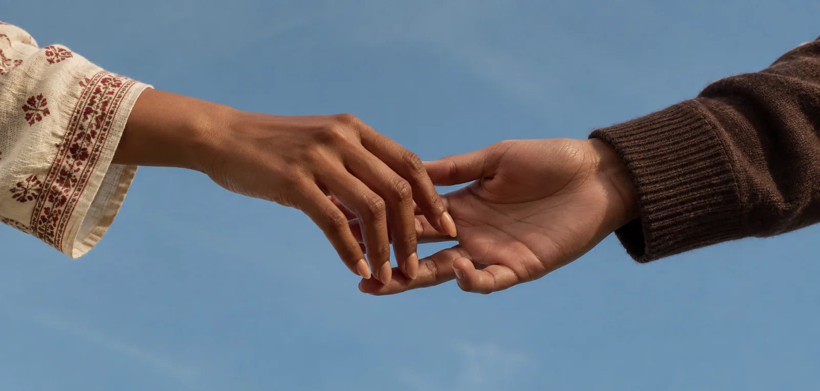 Two hands reaching towards each other against a blue sky.