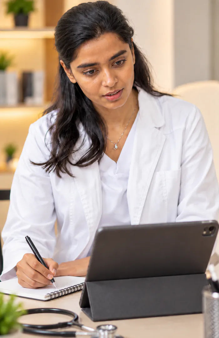 A physician in a white coat writing notes during a video consultation