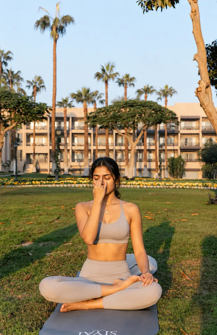A woman seated cross-legged on a lawn practising a breathing exercise