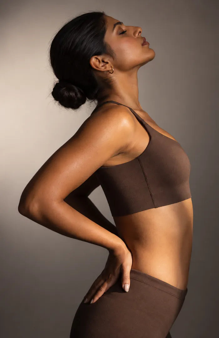 A woman standing in profile with a hand on her lower back