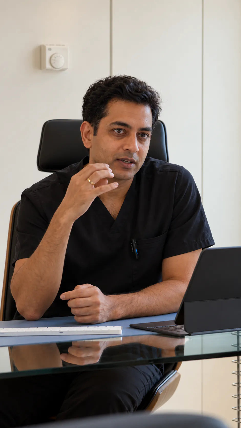 A physician in dark scrubs explaining results at his desk